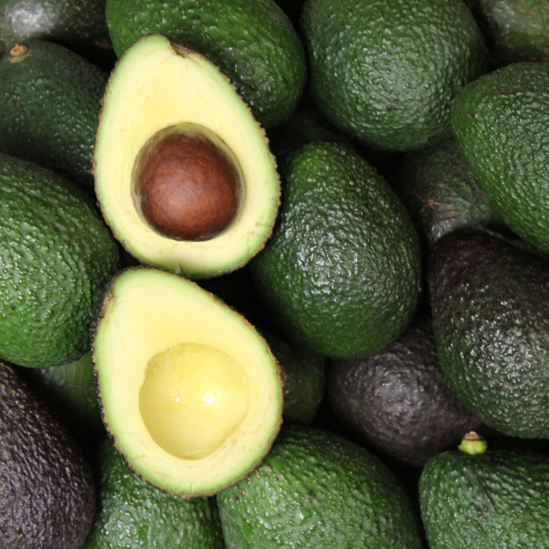A pile of fresh avocados, with one cut in half to show the seed and creamy interior.